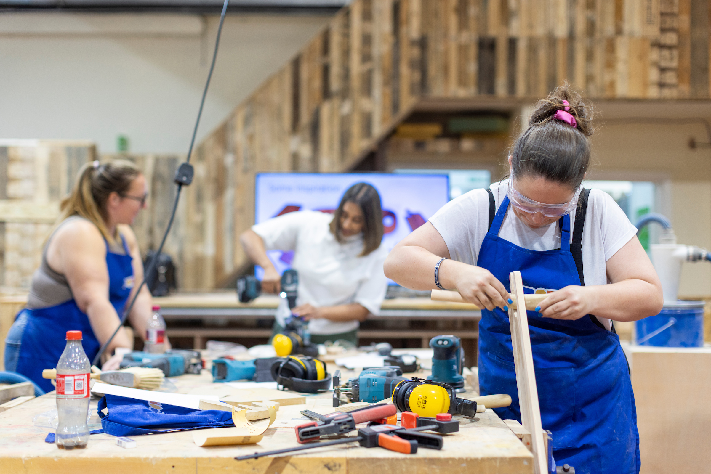 Three women working in a workshop with power tools and timber