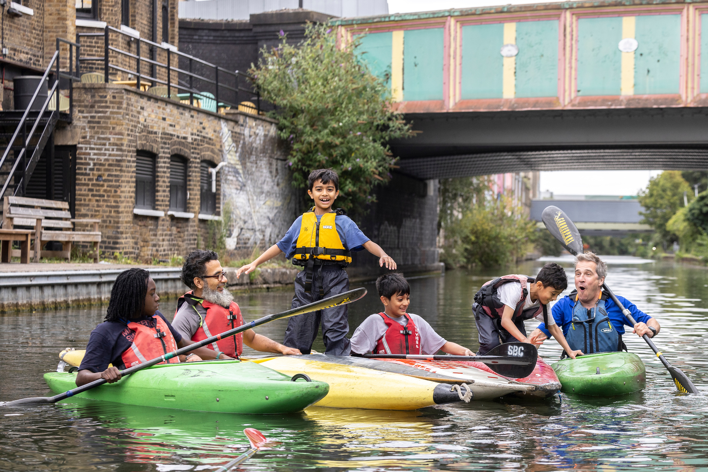 Image of three children and three men in kayaks on the Grand Union Canal