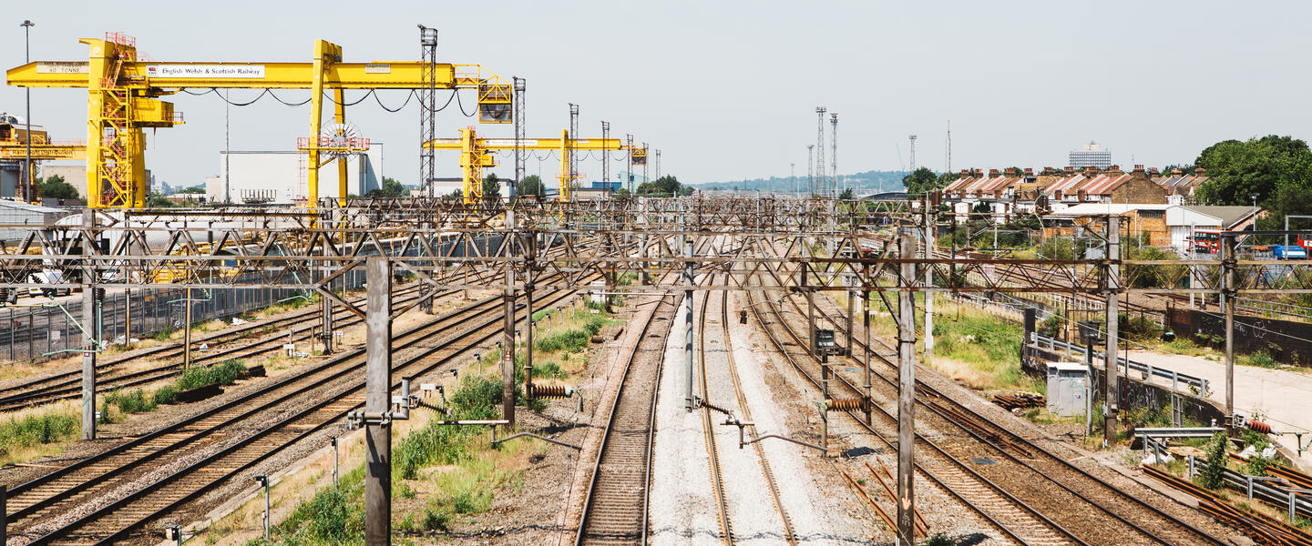 A series of brown rail way lines with yellow cranes to the left