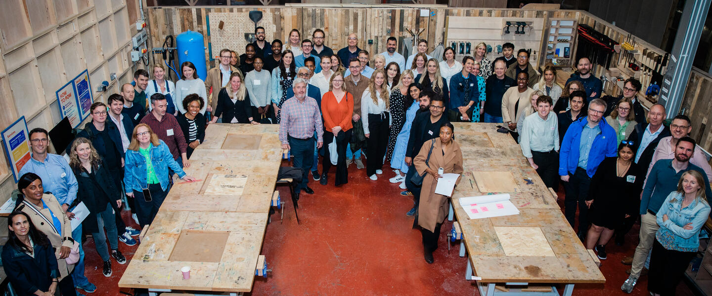 Image of the OPDC staff stood in a large group in a warehouse setting around two large table
