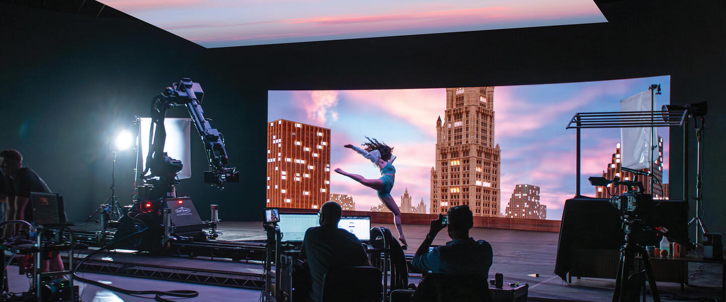 Woman jumping in front of large green screen showing a cityscape
