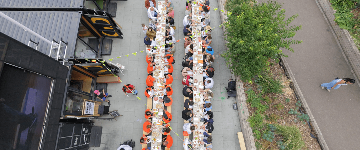 Aerial shot of a large group of people eating at long tables in a square