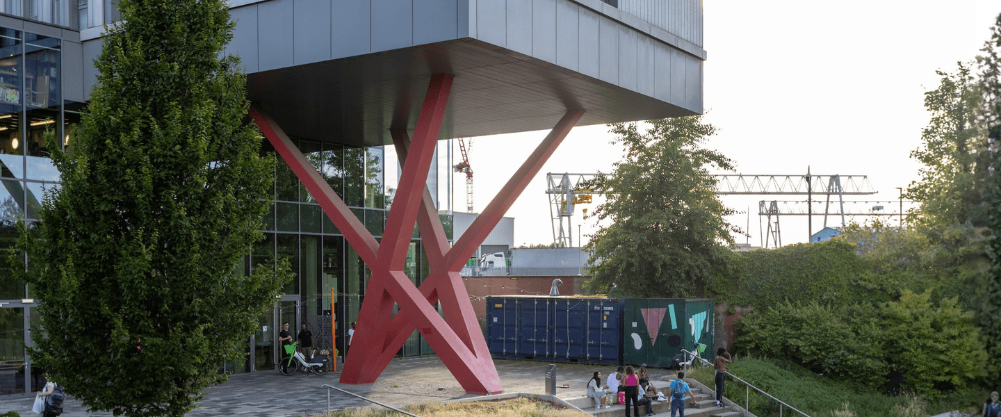 Red metal structure with criss-cross beams holding up a large building alongside a canal