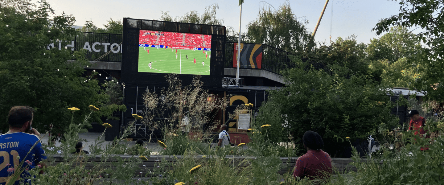 Flowers in front of a large screen in North Acton Square