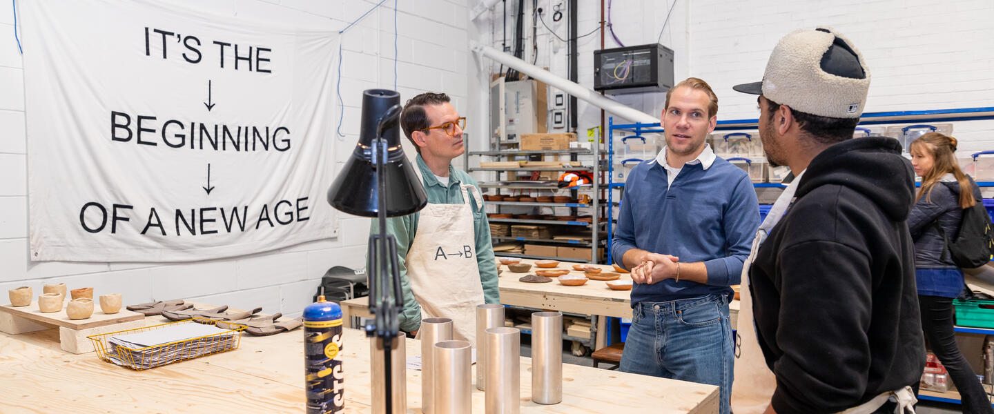 Image of three men, stood around a workbench, chatting. 