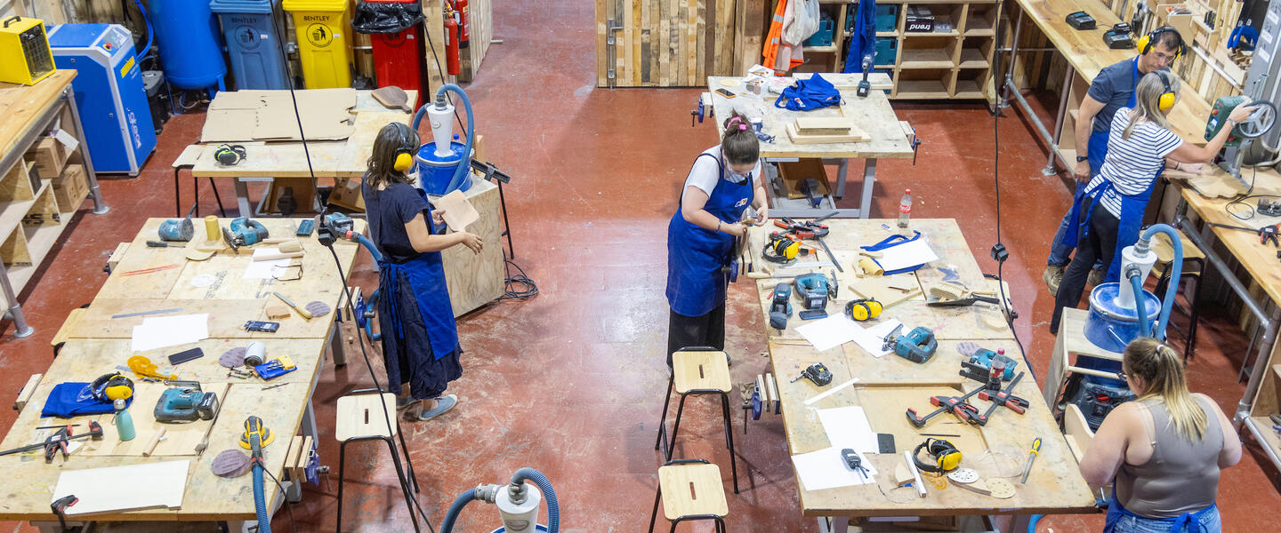 Image of a wood workshop with lots of people working in aprons