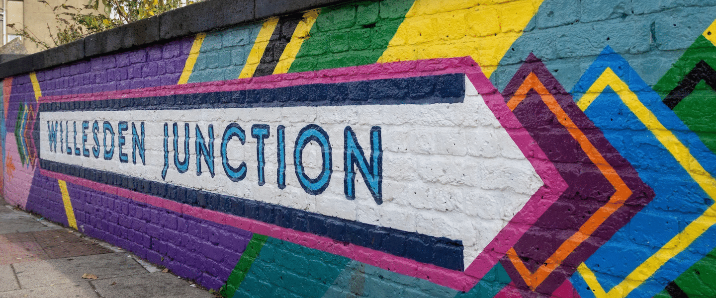 An image of a brightly coloured mural on a short brick wall, which says Willesden Junction