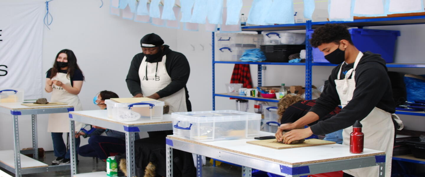 Image of three people in black t-shirts and aprons, working with clay in a workshop