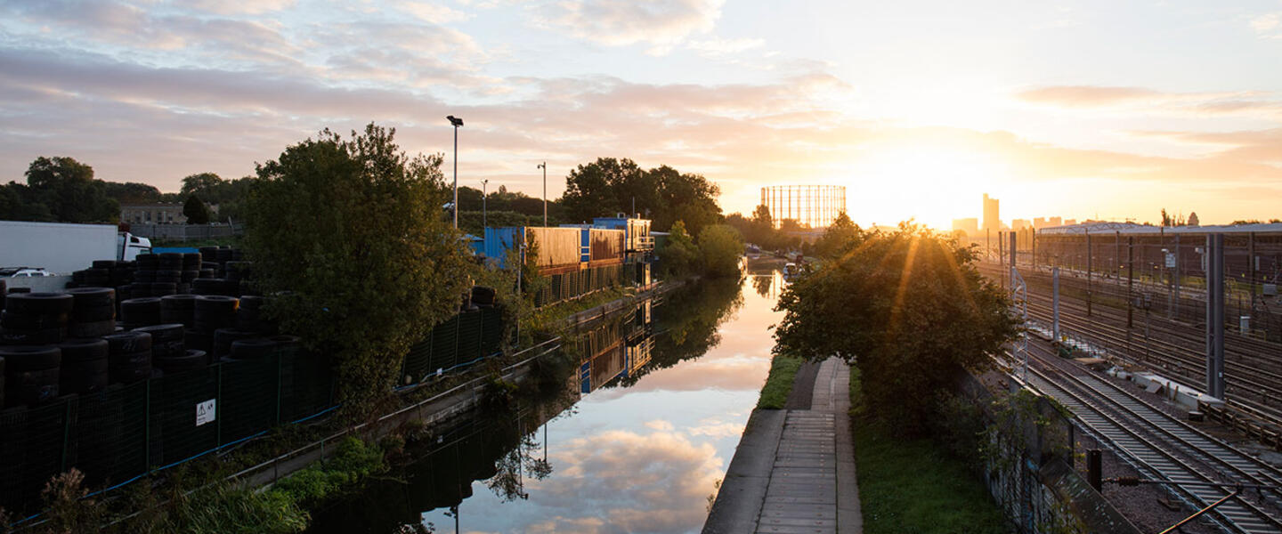 Canal side view with train tracks to the right and the sun going down in the background
