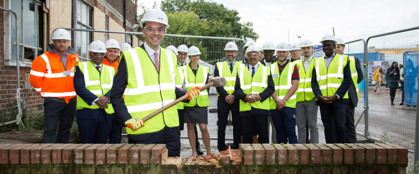 Image of a group of people in high vis jackets and the deputy mayor, James Murray, knocking down some bricks